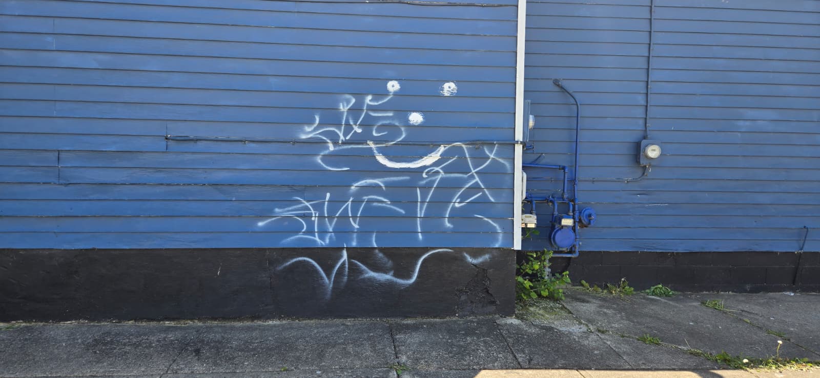White spray paint graffiti on blue building siding